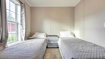 A room with two single beds, a nightstand with drawers, a window with curtains, and a view of a red building outside.