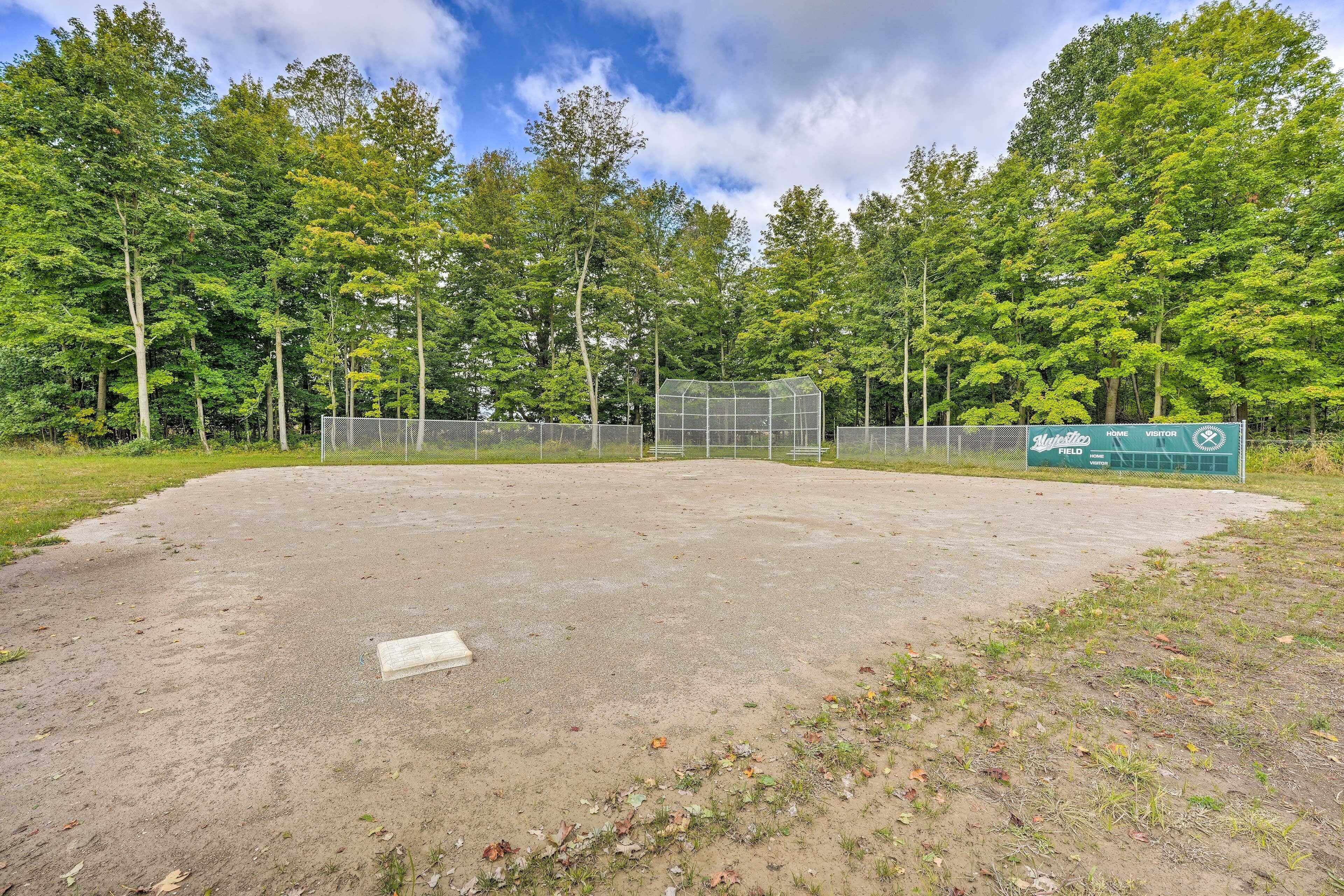 A baseball field with a green sign, trees, and a clear sky.