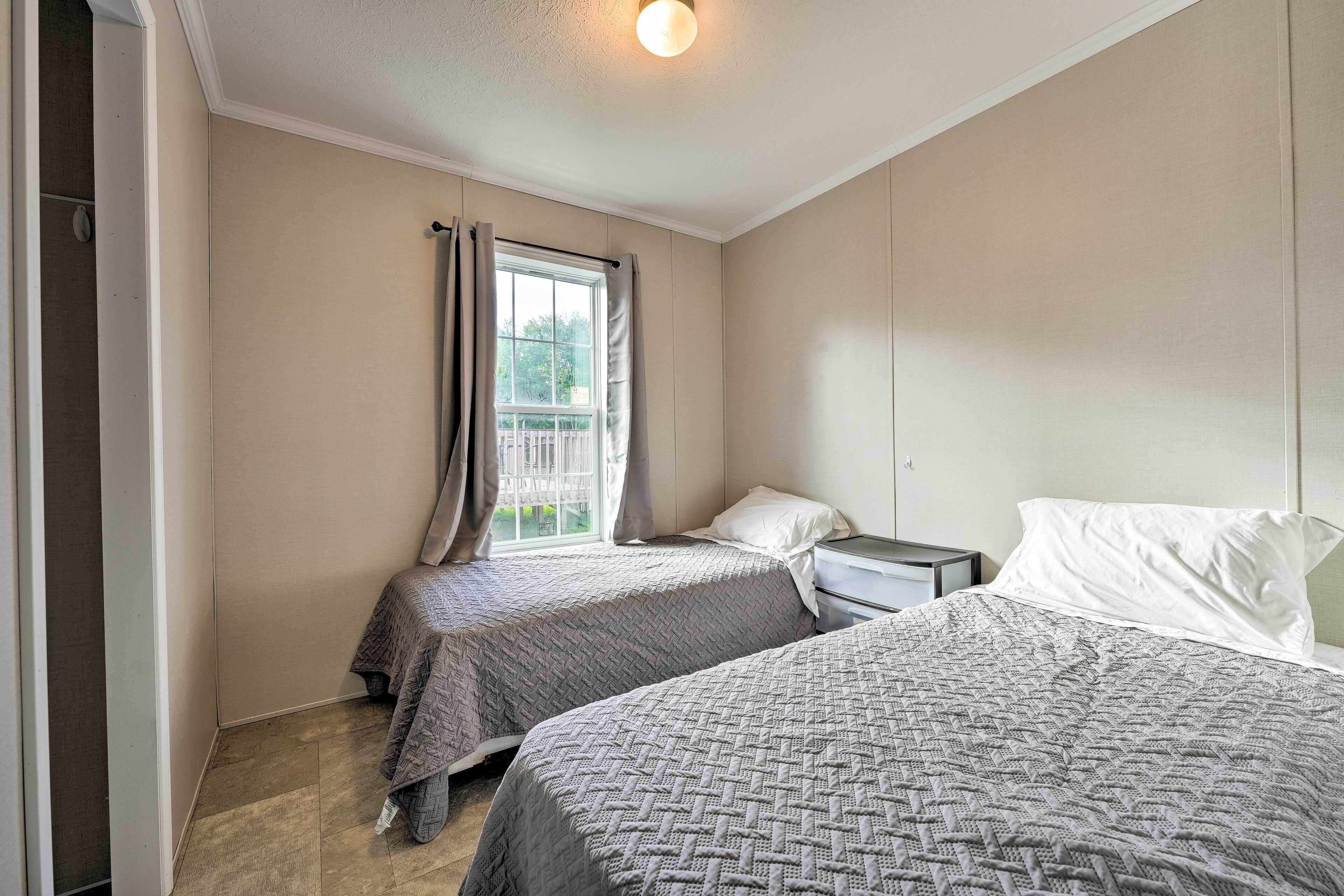A bedroom with two beds, a window with curtains, a bedside table, and a nightstand.