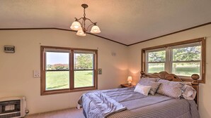 A bedroom with a large bed, two windows, a ceiling fan, and a nightstand with a lamp. - Charming Burdett Home With Grill, Gazebo + Yard (Burdett)