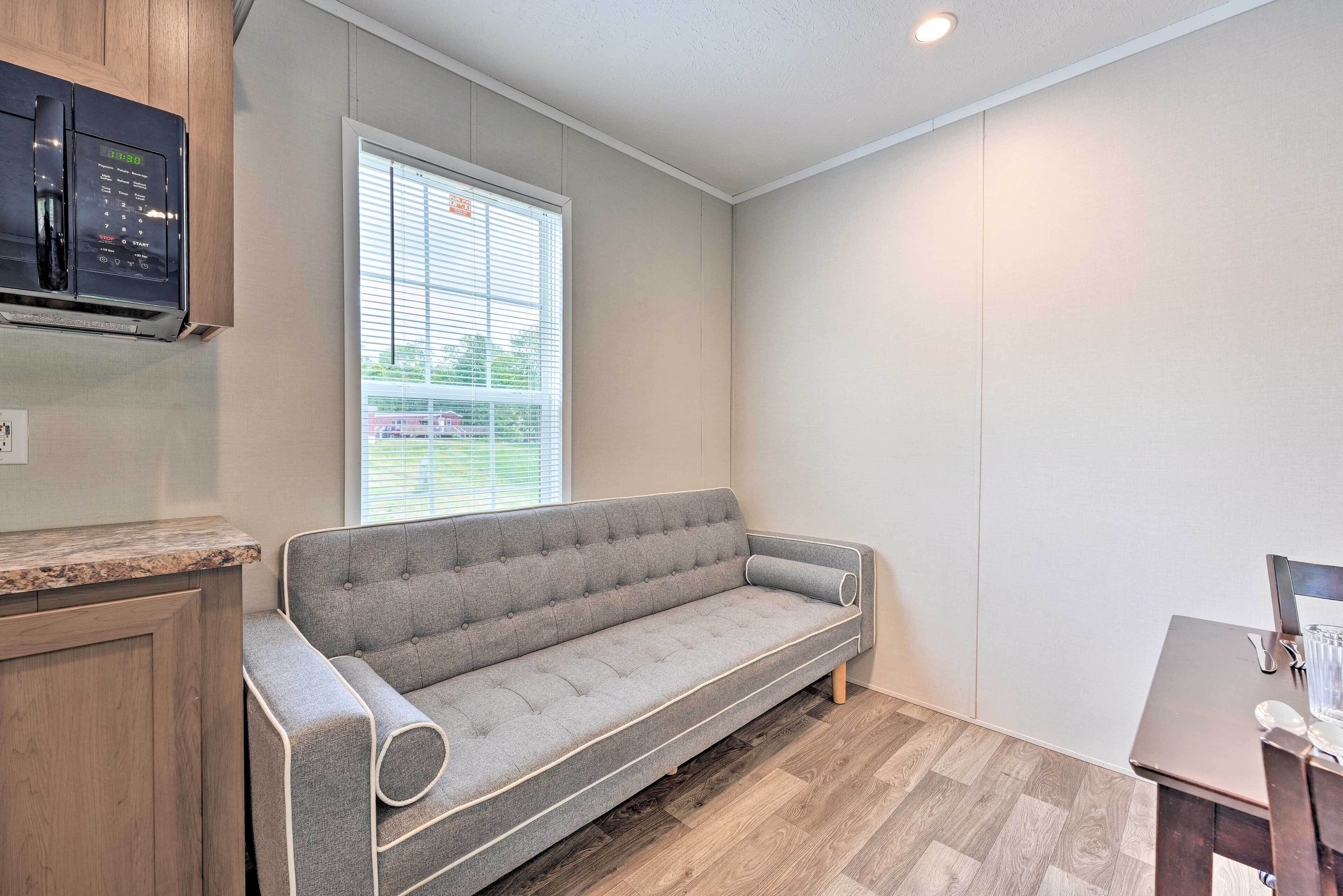 A compact living space with a sofa, a microwave, and a window with blinds.