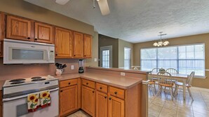 A kitchen with wooden cabinets, a microwave, stove, and a dining area with a table and chairs.
