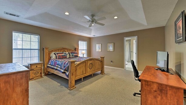 A bedroom with a wooden bed, a desk, a chair, a ceiling fan, and two windows.