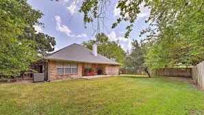 A single-story brick house with a covered porch, a fenced yard, and mature trees.