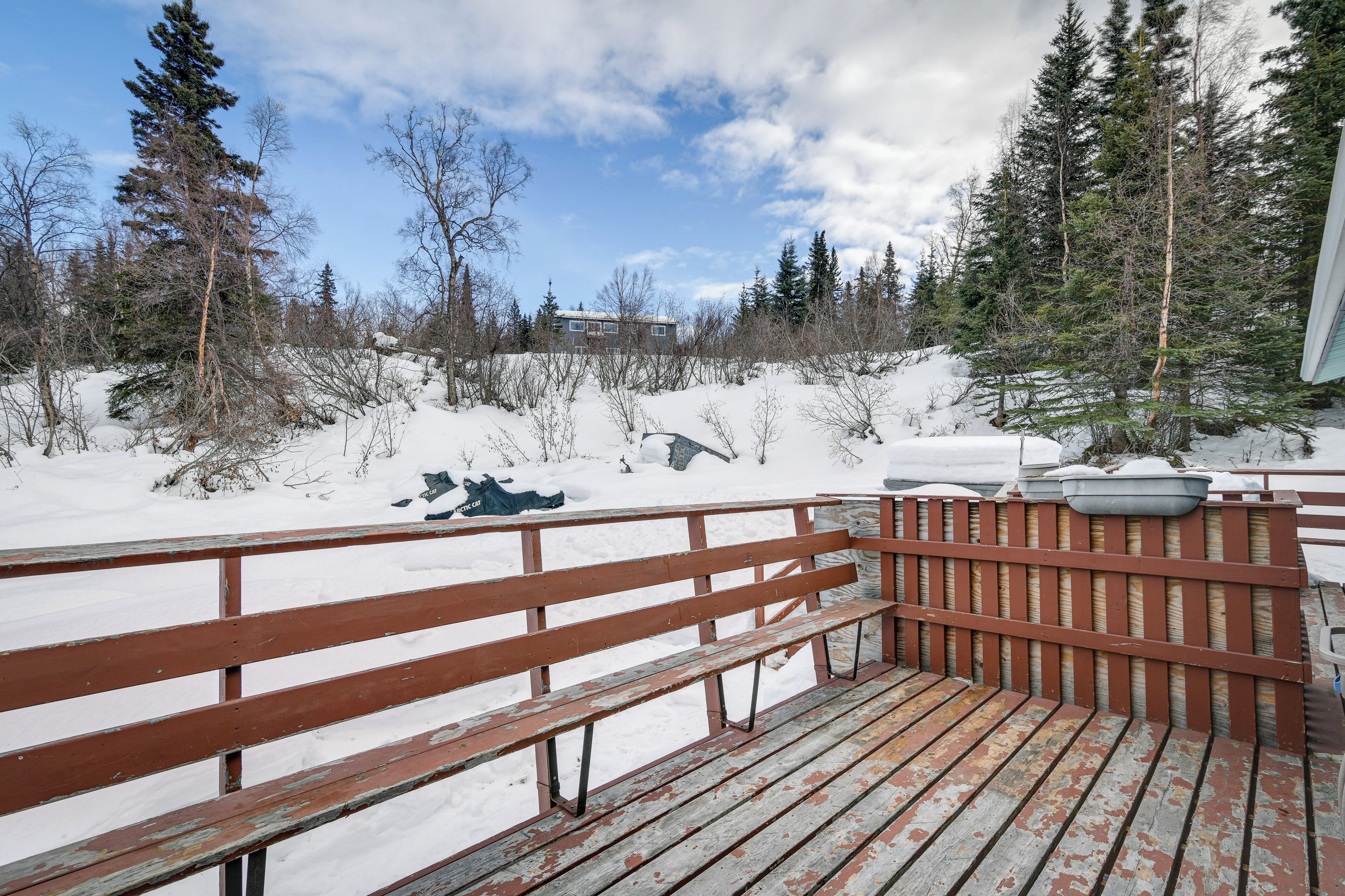 Une terrasse en bois avec des bancs, entourée d’un paysage enneigé et d’arbres.
