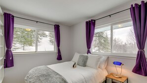 Ein Schlafzimmer mit Bett, Nachttisch, Lampe und violetten Vorhängen.