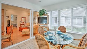 A dining area with a glass table, wicker chairs, and a television on a stand.