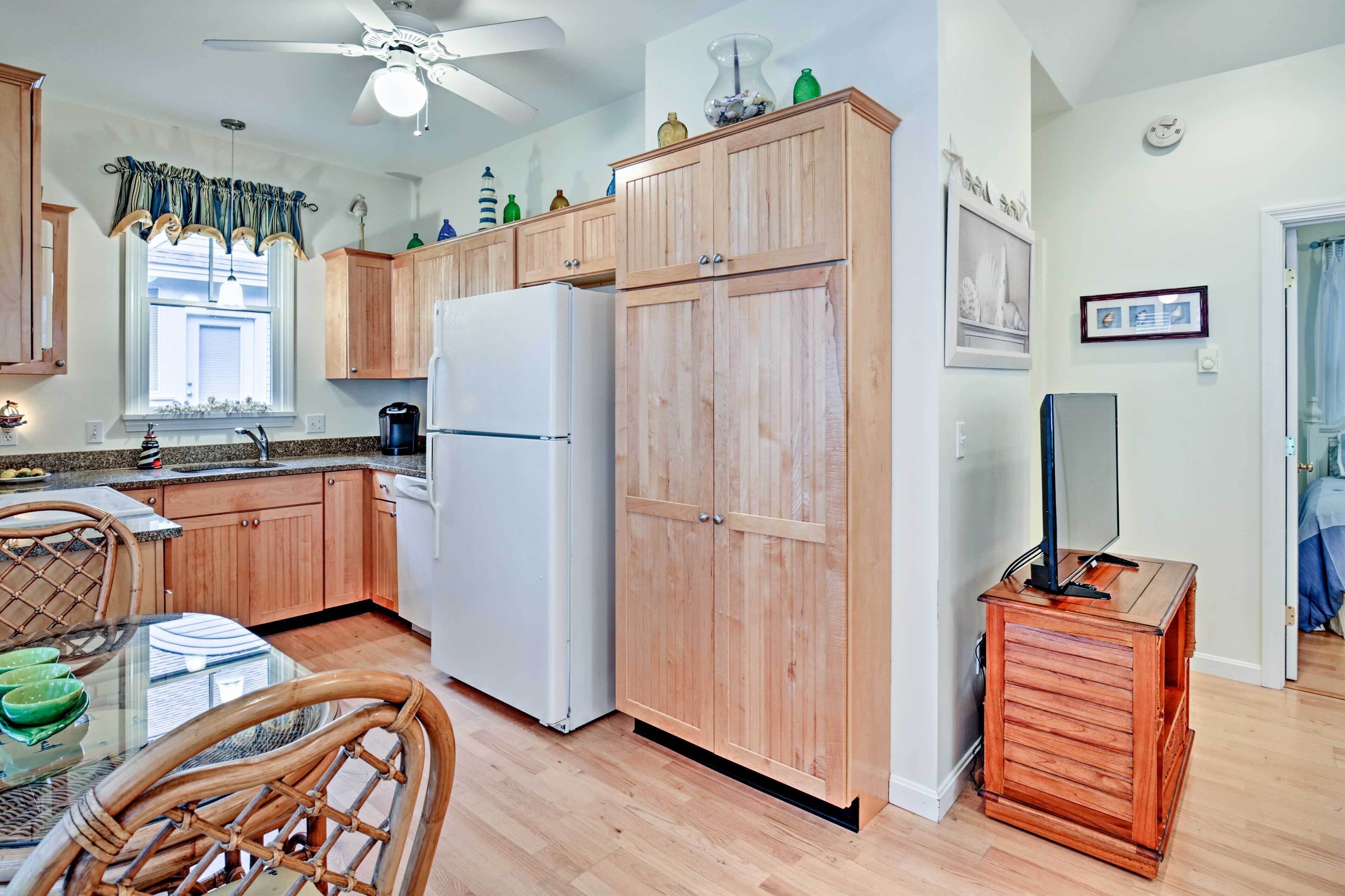 Una cocina con armarios de madera, un refrigerador blanco, una mesa de comedor con sillas y un ventilador de techo.