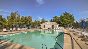 A swimming pool with lounge chairs and umbrellas, surrounded by trees and a building.