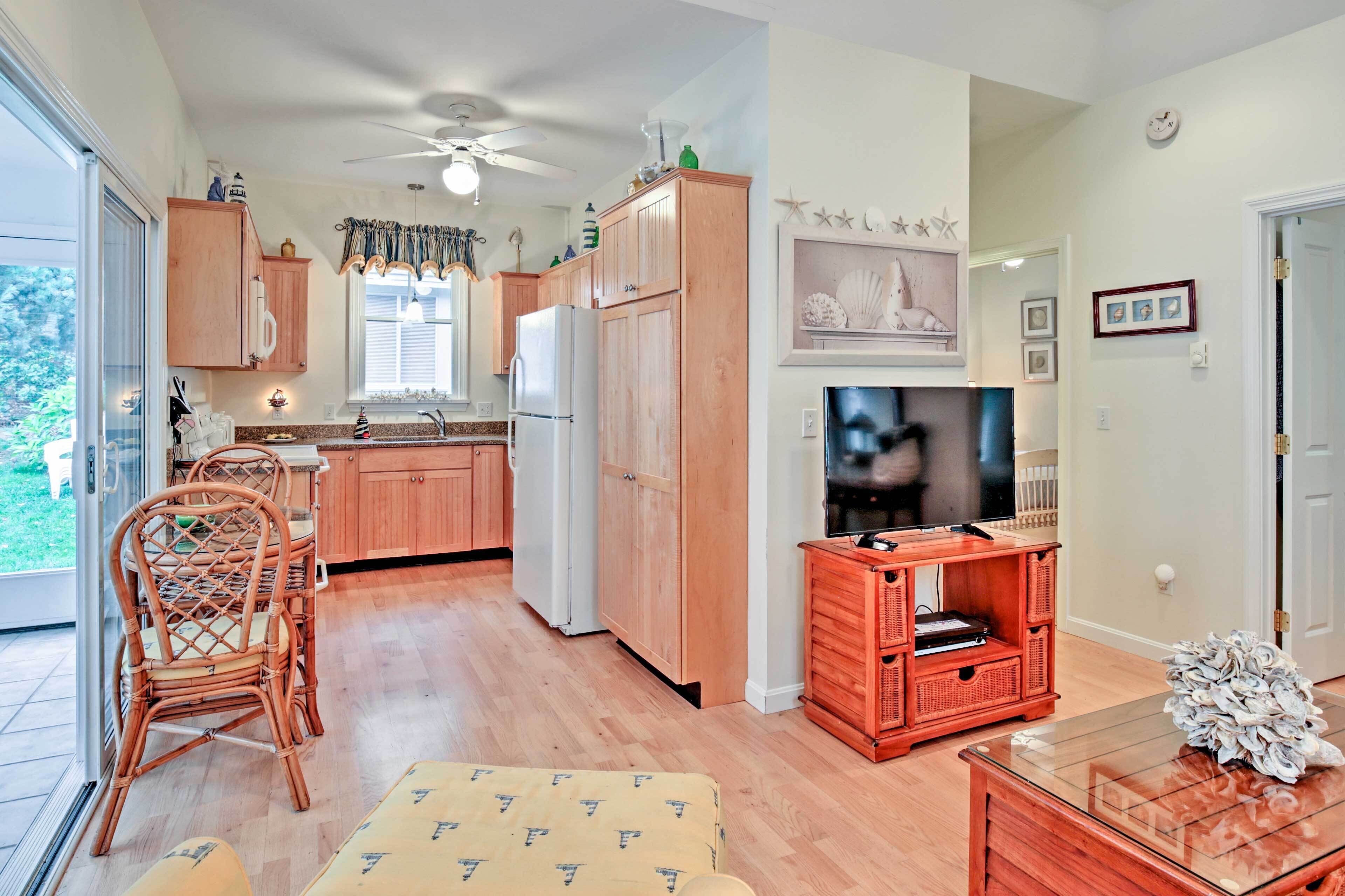 A compact kitchen with wooden cabinets, a refrigerator, and a dining area with wicker chairs.