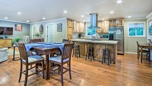 Una cocina amplia con armarios de madera, una isla grande con taburetes, un refrigerador de acero inoxidable y un comedor con mesa y sillas.