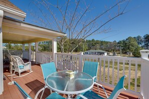 A covered outdoor patio with a round glass table, blue chairs, and a rocking chair. - Welcoming Cottage w/ Outdoor Pool & Water Views! (White Stone)