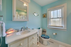 A bathroom with a sink, mirror, toilet, and window. - Welcoming Cottage w/ Outdoor Pool & Water Views! (White Stone)