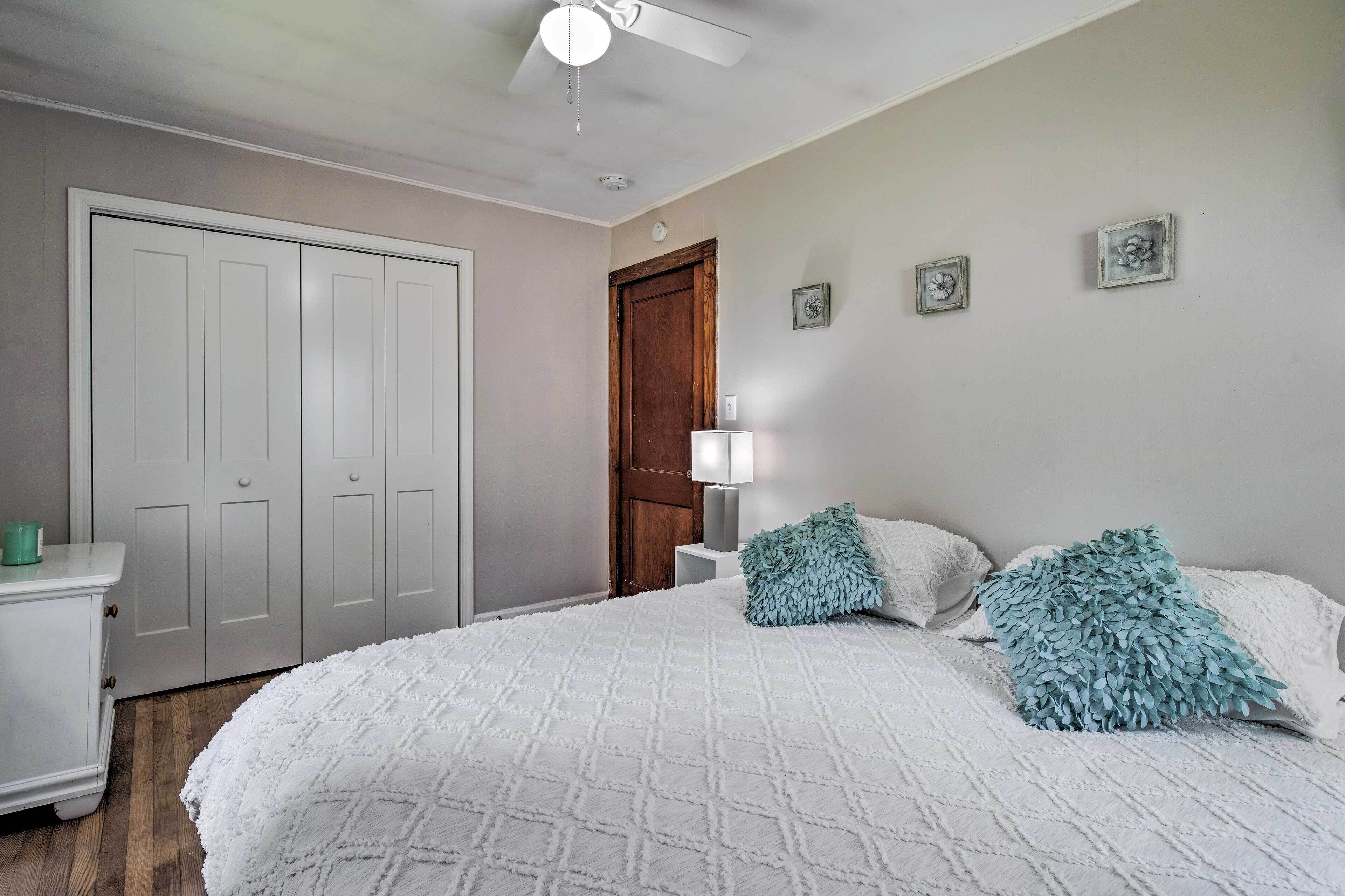A bedroom with a large bed, a wardrobe, a nightstand with a lamp, and a ceiling fan.