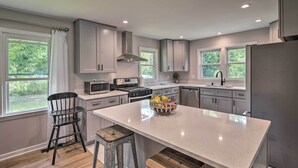 Une cuisine moderne avec des meubles gris, un îlot central et une vue sur la verdure à l’extérieur.