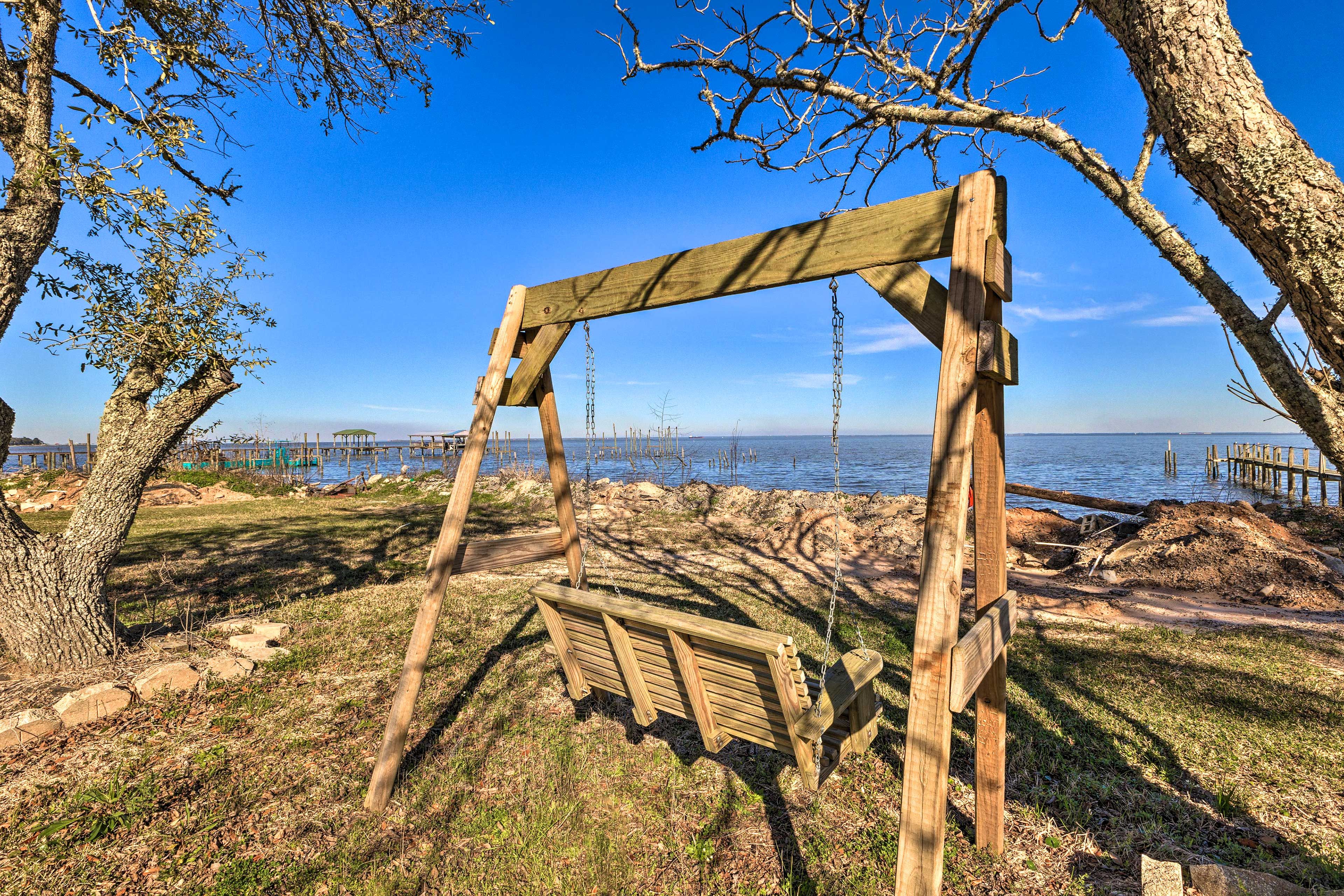A wooden swing set in a park with a view of the water and distant structures.