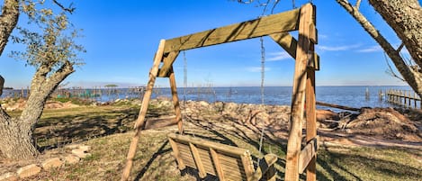 A wooden swing set in a park with a view of the water and distant structures.