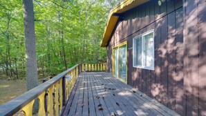 A wooden cabin with a deck, surrounded by trees. - Cozy Adirondacks Cabin: Walk to Lake Eaton! (Jay)