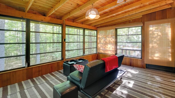 A cozy cabin interior with a wooden ceiling, large windows, a sofa, and a small table. - Cozy Adirondacks Cabin: Walk to Lake Eaton! (Jay)