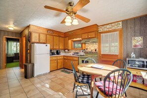 Una cocina con gabinetes de madera, un ventilador de techo, un refrigerador, una mesa de comedor con sillas y un microondas.