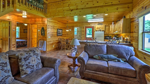 Interior de una cabaña de madera con sala de estar, comedor y cocina.