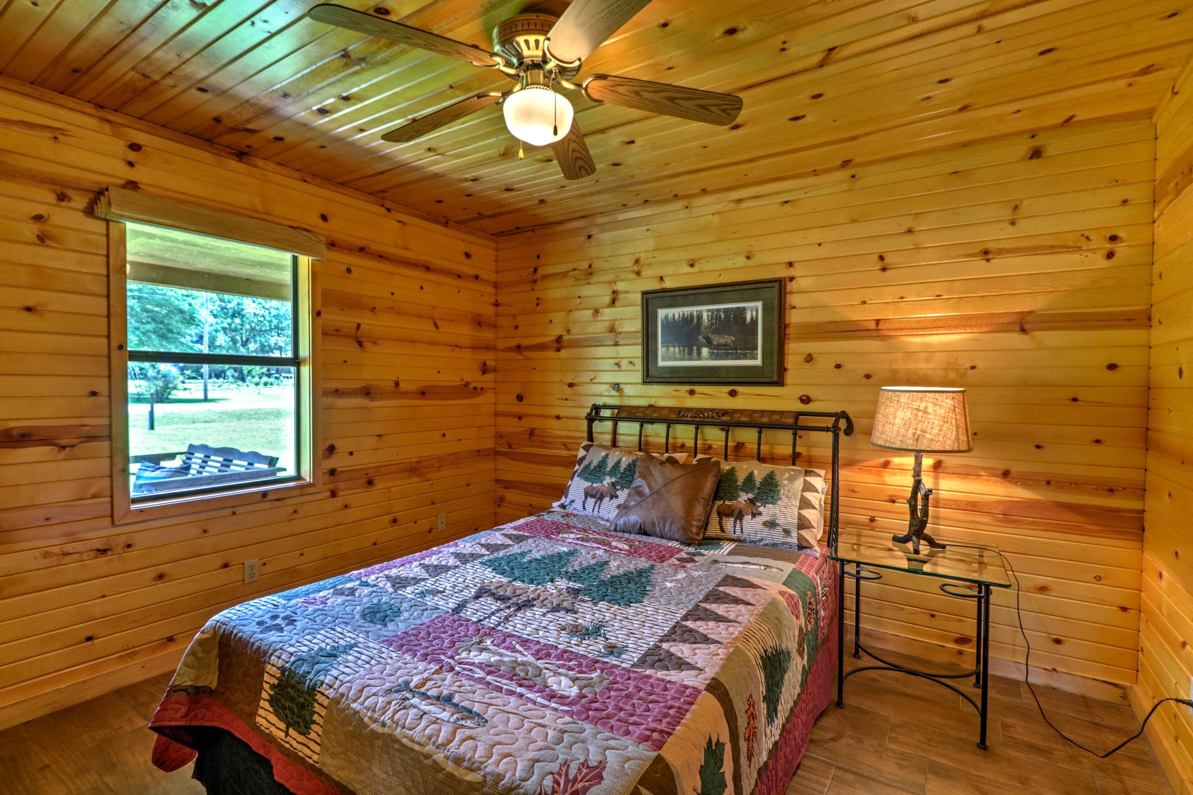 Una habitación de cabaña de madera con una cama, un ventilador de techo, una ventana y un cuadro en la pared.