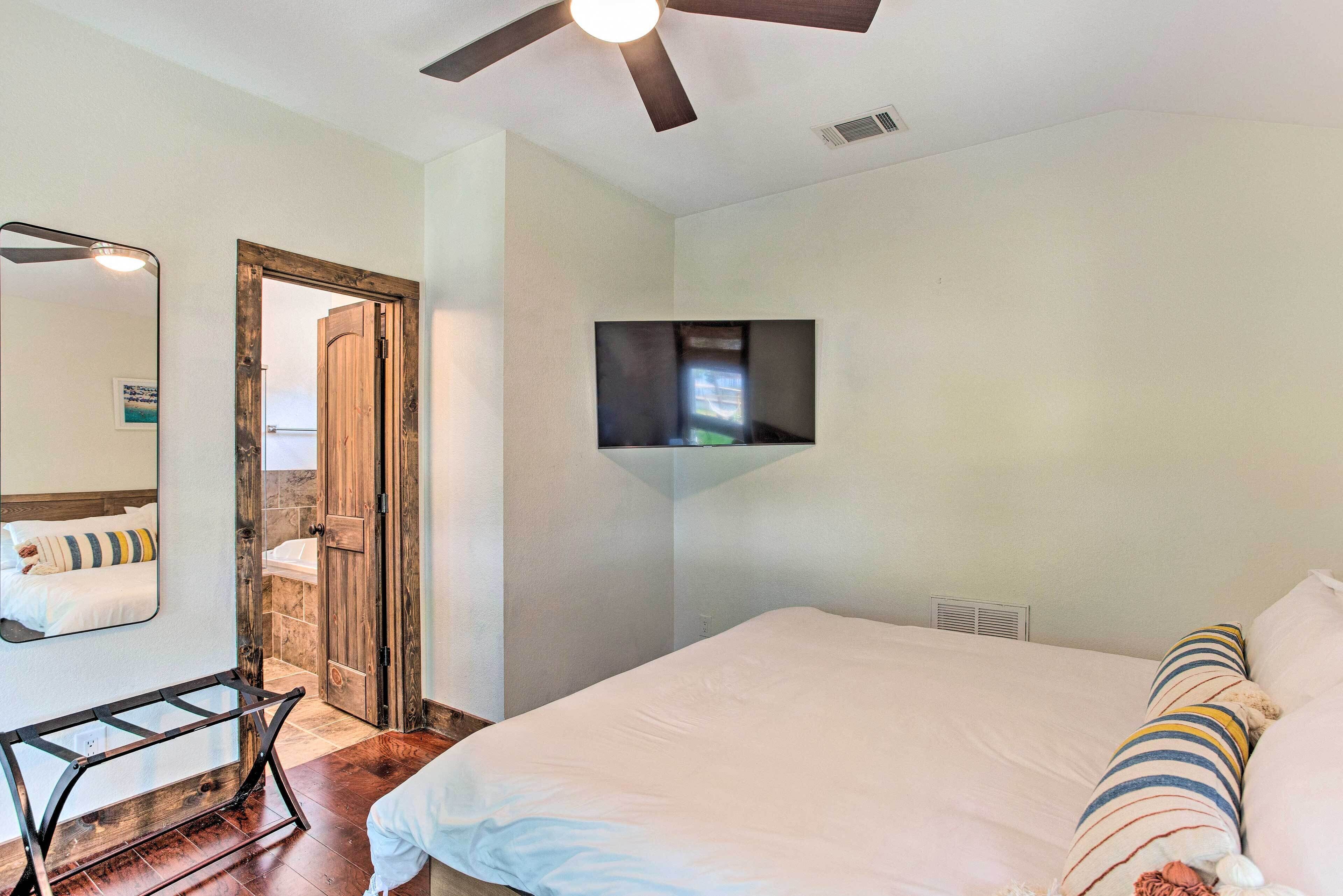 A bedroom with a bed, a TV mounted on the wall, a ceiling fan, and a wooden door.