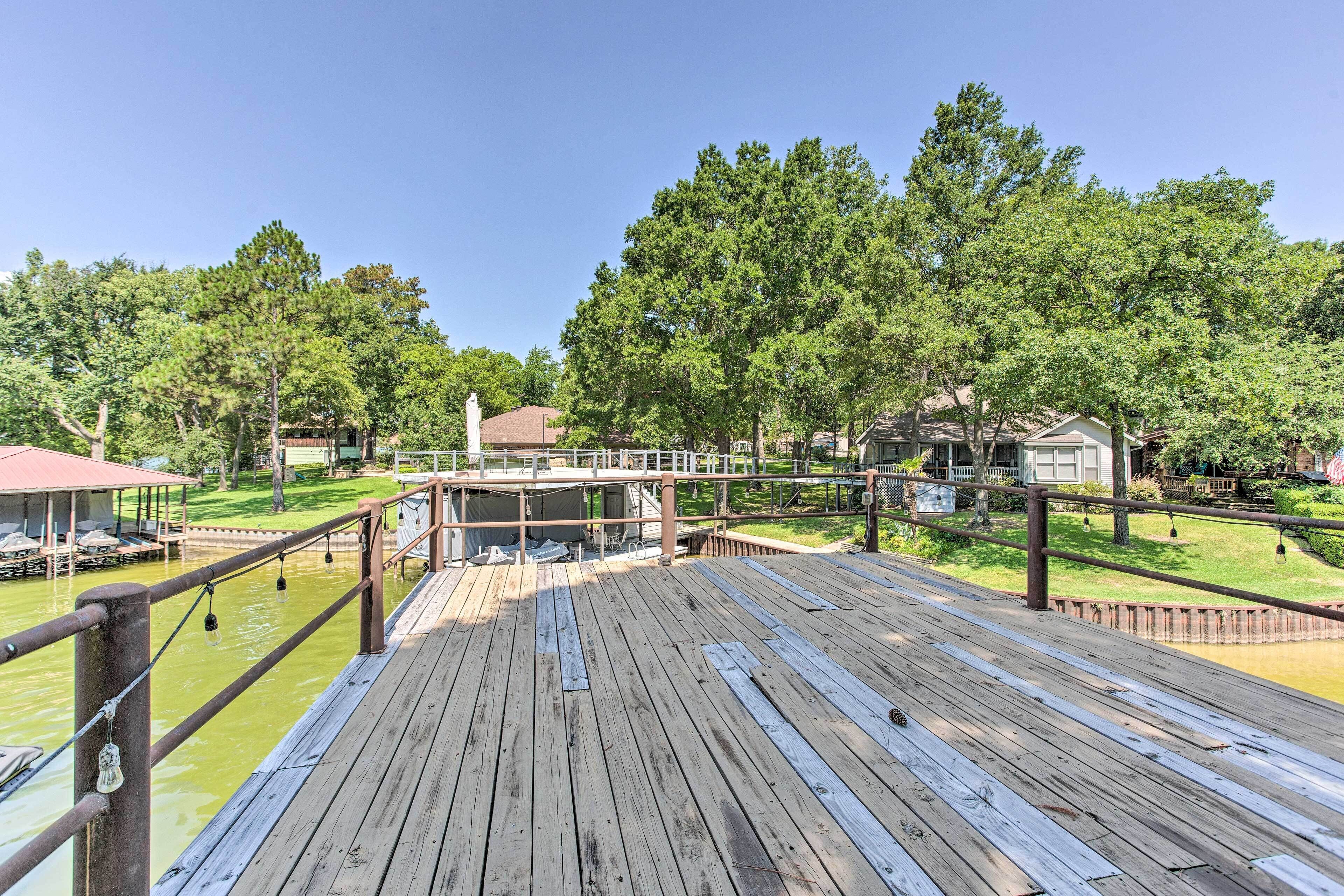 A wooden deck with a railing, overlooking a body of water and a grassy area with trees.