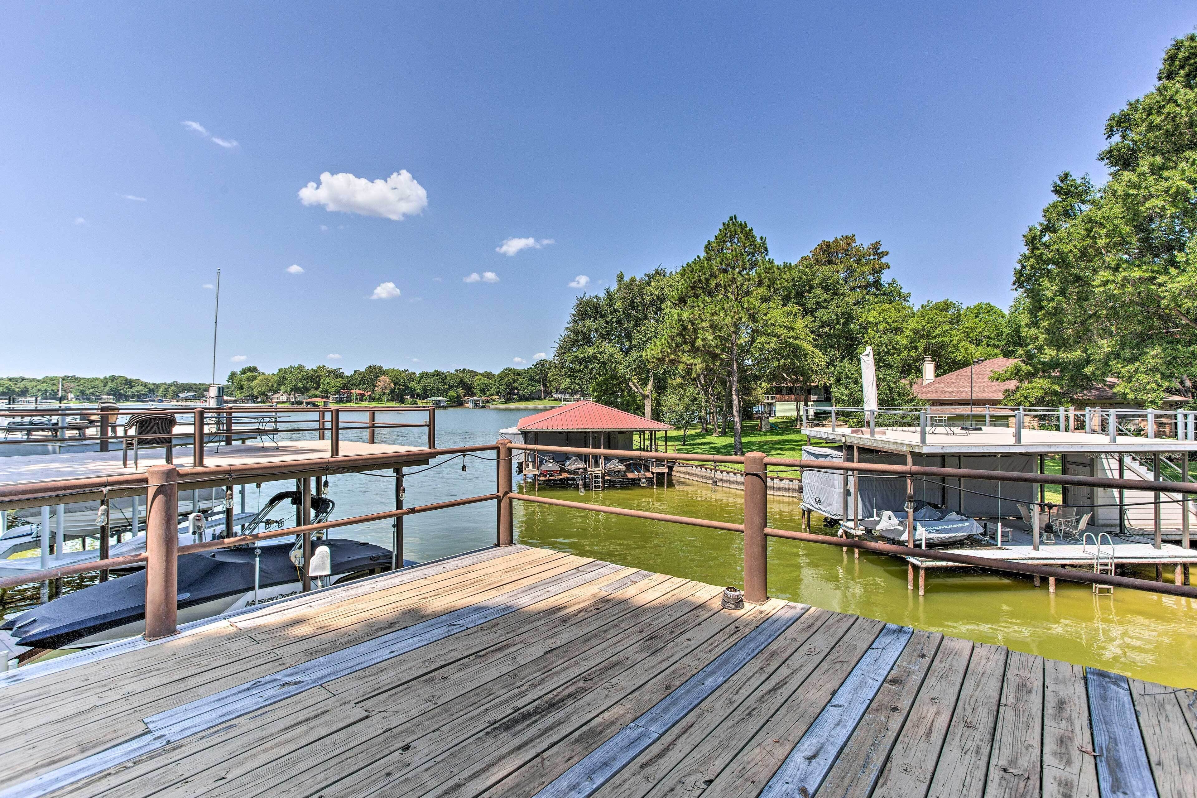 A wooden dock with boats, a covered seating area, and a view of a lake surrounded by trees.