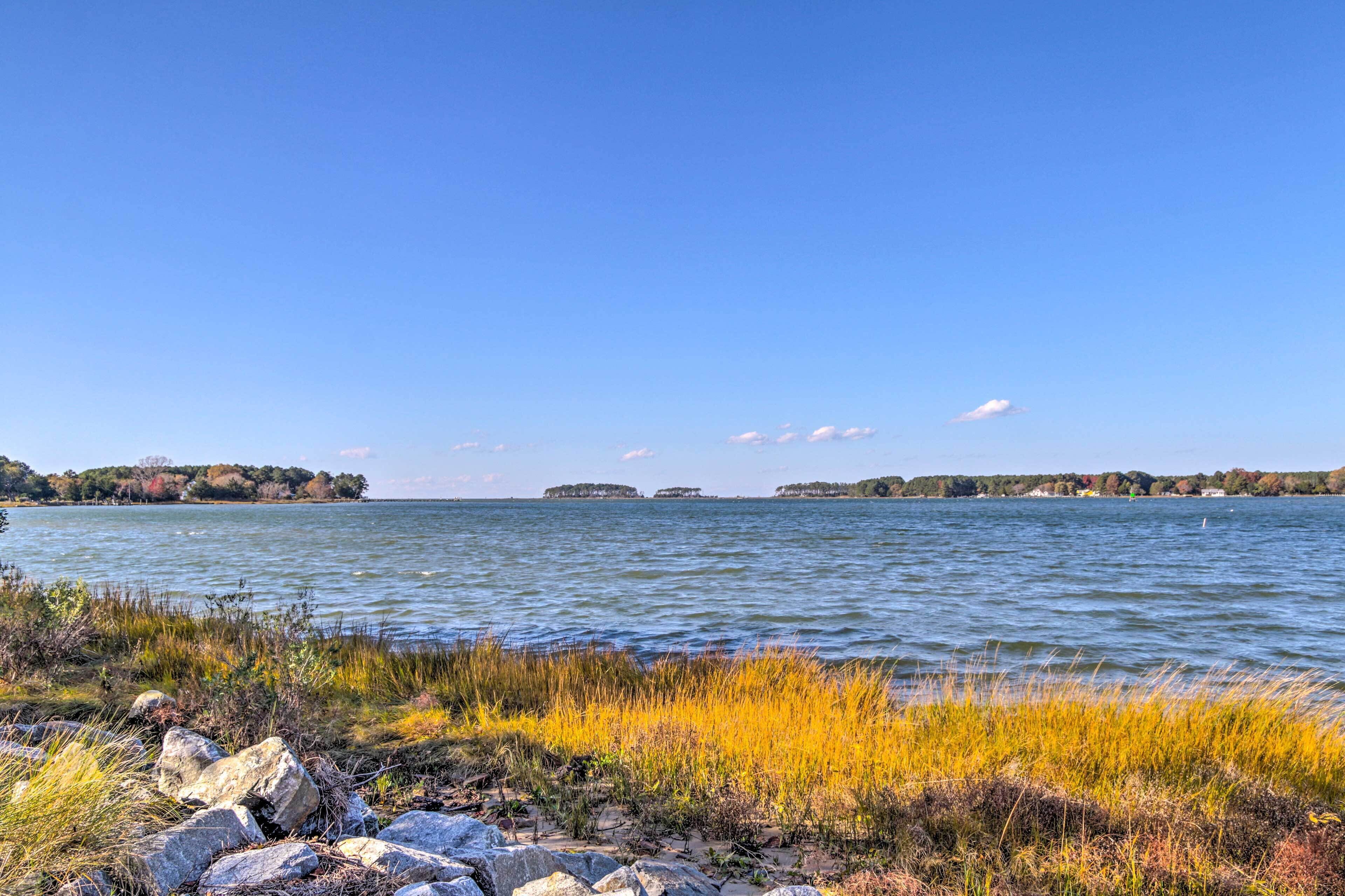 A calm lake with visible islands in the distance, surrounded by grassy areas and rocks.