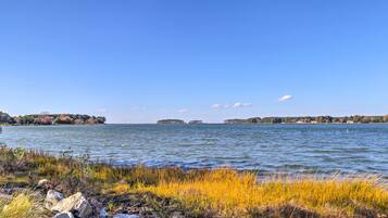A calm lake with visible islands in the distance, surrounded by grassy areas and rocks.