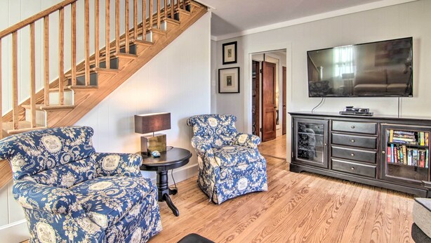 A living room with a wooden staircase, patterned armchairs, a small table with a lamp, a television, and a bookshelf. - 'cora's Cottage' Near Chesapeake Bay Access! (Harborton)