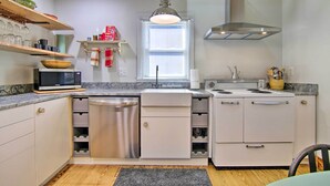 A compact kitchen with a microwave, dishwasher, stove, and wooden shelves. - 'cora's Cottage' Near Chesapeake Bay Access! (Harborton)