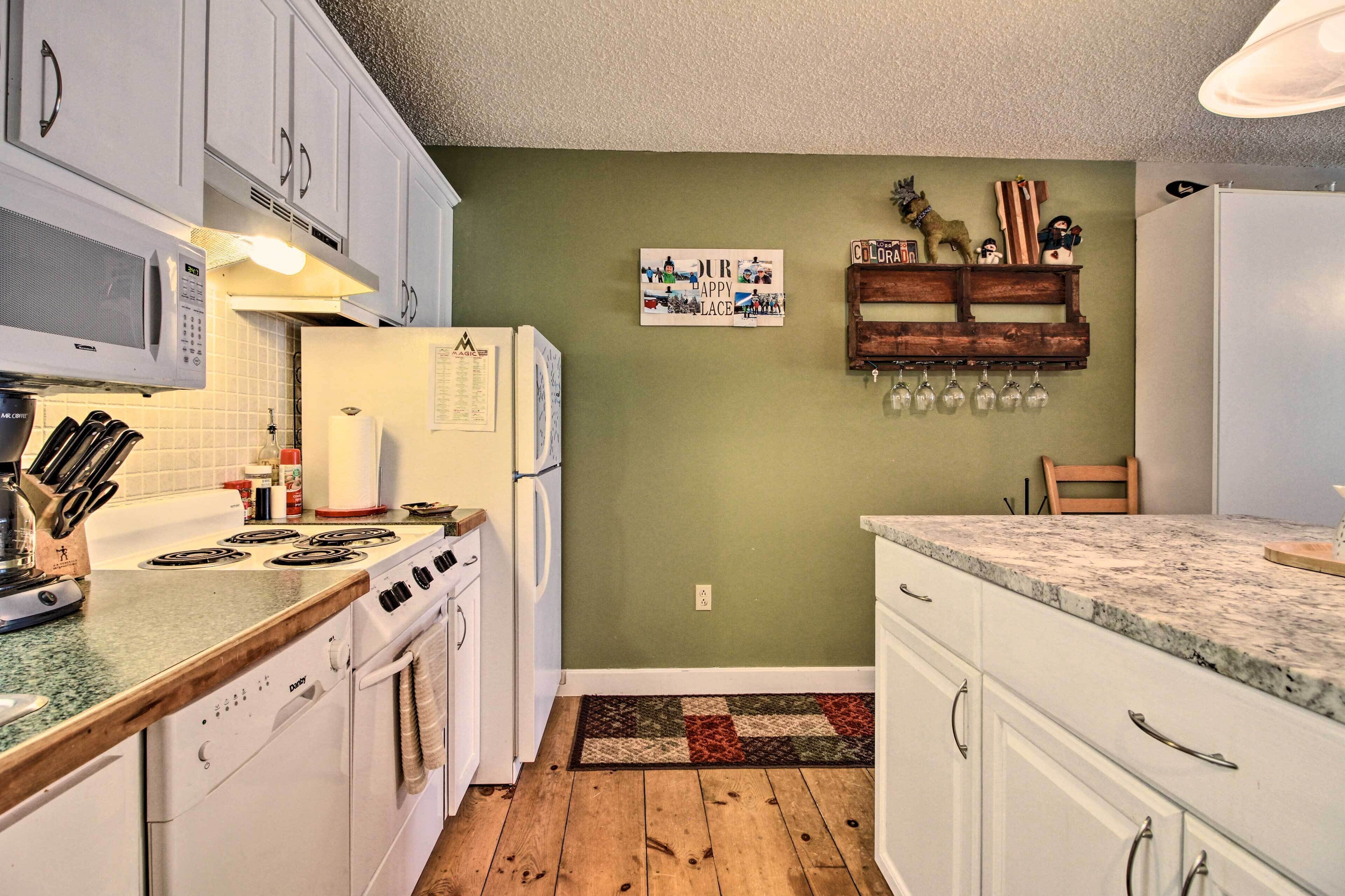 A kitchen with white cabinets, a microwave, a stove, and a refrigerator. There is a wooden floor and a green wall.