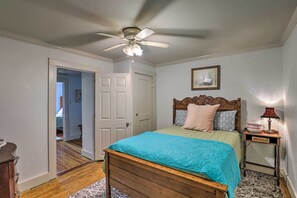 A bedroom with a wooden bed, a ceiling fan, a nightstand with a lamp, and a door leading to another room. - Cozy Hendersonville Home Near Trails + Parks! (Hendersonville)