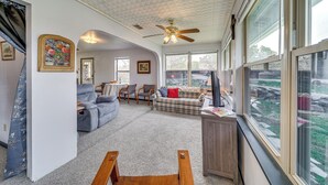 A spacious living room with a ceiling fan, large windows, a sofa, a coffee table, and a desk. - Cozy Kerrville Guest Cottage Near Guadalupe River! (Kerrville)