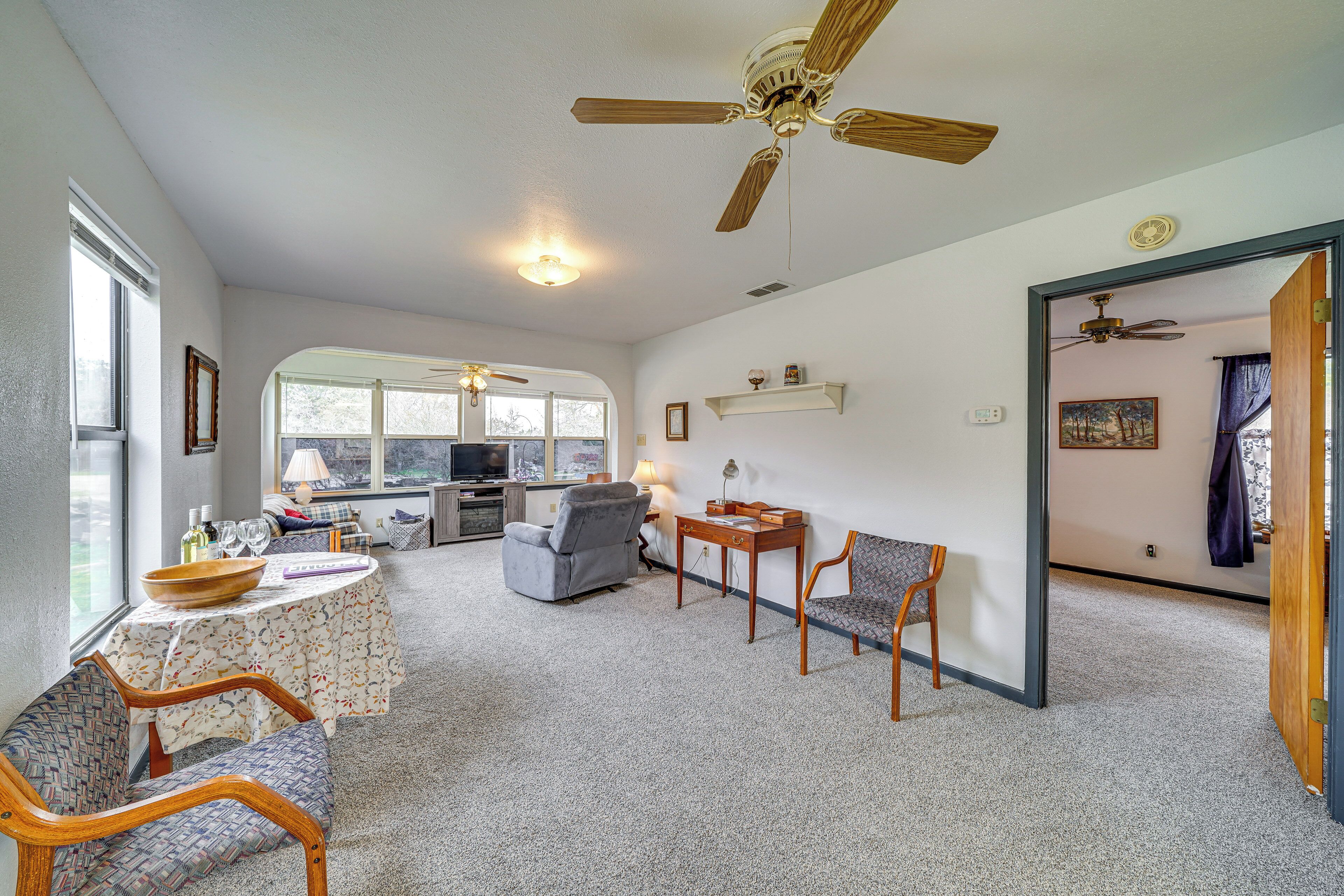 A spacious living room with a ceiling fan, a dining area with a table and chairs, and a kitchen in the background.