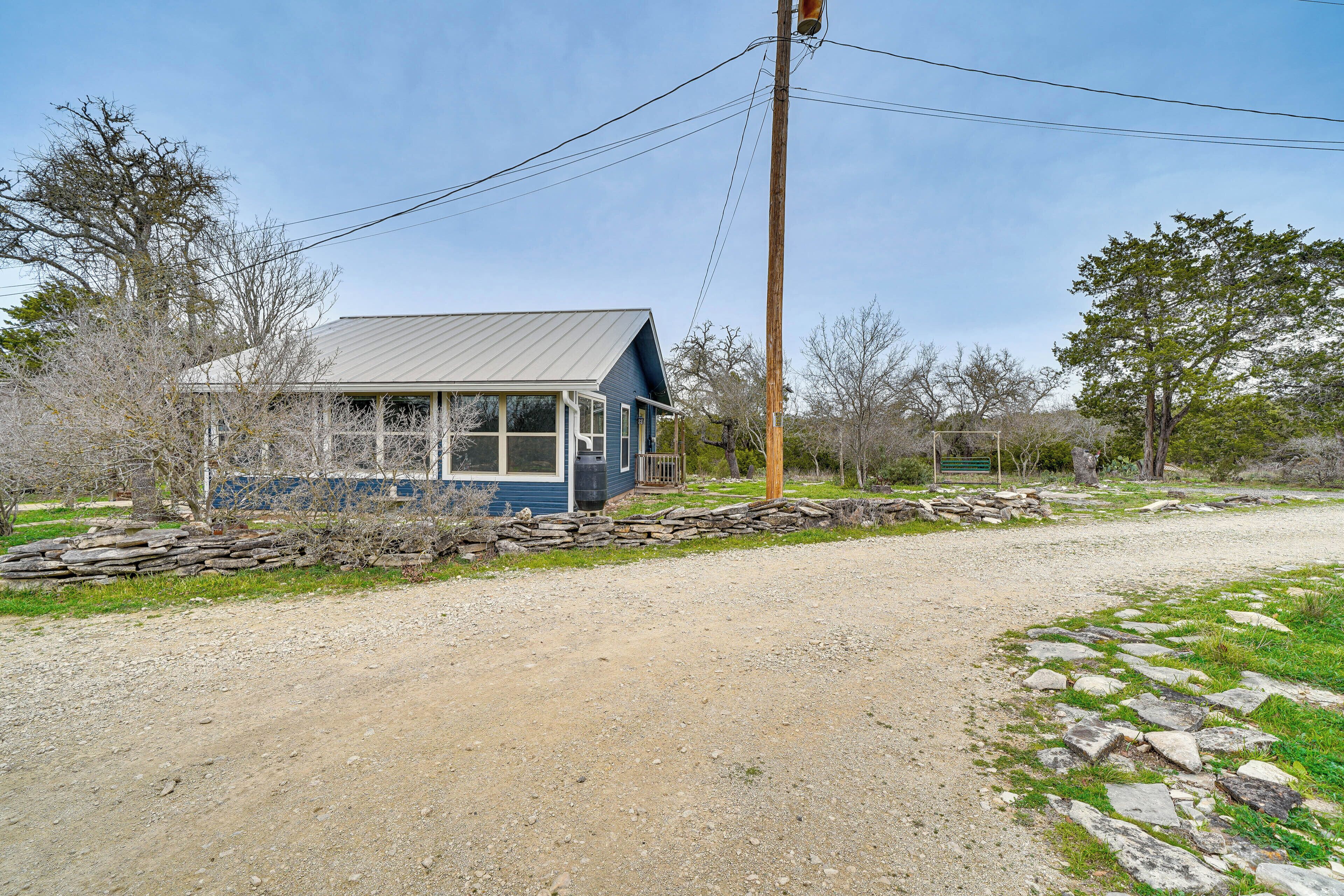A house with a metal roof and stone wall foundation, surrounded by a gravel driveway and sparse vegetation.