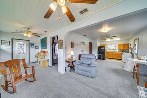 A spacious living room with a wooden rocking chair, a gray armchair, and a dining table with chairs. There is a kitchen area with wooden cabinets and a refrigerator. - Cozy Kerrville Guest Cottage Near Guadalupe River! (Kerrville)