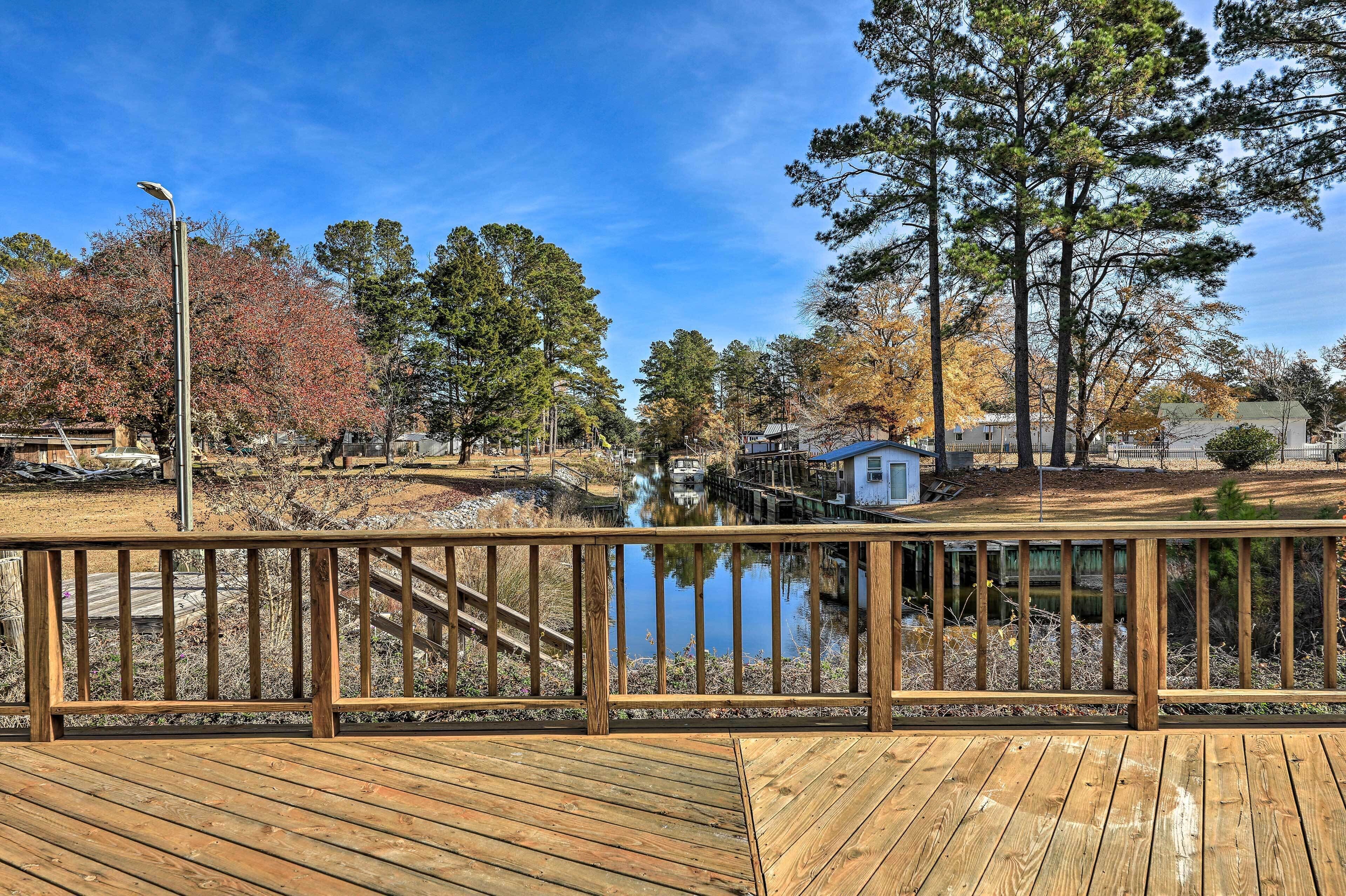 A wooden deck with a view of a lake, trees, and a small dock.