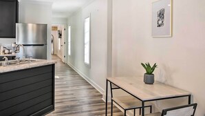Une cuisine moderne avec un réfrigérateur en acier inoxydable, un plan de travail noir et une table à manger en bois accompagnée d’une chaise.