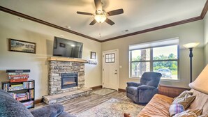 A living room with a stone fireplace, a ceiling fan, a television, and a bookshelf. - Cozy Townsend Condo, Resort-style Amenities! (Townsend)