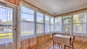 A sunroom with wooden walls and floor, large windows with sheer curtains, a wooden table, and two chairs. - Family-friendly Marlinton Home: Walk Downtown! (Marlinton)
