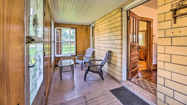 A covered porch with wooden flooring, two Adirondack chairs, and a glass door leading to a room. - Family-friendly Marlinton Home: Walk Downtown! (Marlinton)