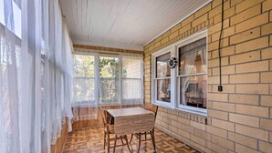 A room with a wooden floor, a table, chairs, a window with a curtain, and a brick wall. - Family-friendly Marlinton Home: Walk Downtown! (Marlinton)