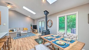 Un salon moderne comprenant un coin repas, un plancher en bois, une cheminée et de grandes fenêtres donnant sur l’extérieur.