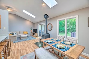 A modern living room with a dining area, wooden flooring, a fireplace, and large windows offering a view of the outdoors.