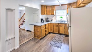 A kitchen with wooden cabinets, a white refrigerator, and a built-in island with a sink. - Cozy Ishpeming Cottage w/ Lake & Park Views! (Ishpeming)