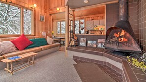 A cozy cabin interior with a fireplace, wooden walls, a sofa with cushions, and a dining area. - Walk to Ski Trails: Ludlow Home on Okemo Mountain! (Ludlow)
