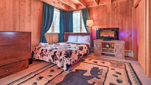 A wooden cabin bedroom with a bed, a nightstand, a lamp, and a TV. - Walk to Ski Trails: Ludlow Home on Okemo Mountain! (Ludlow)